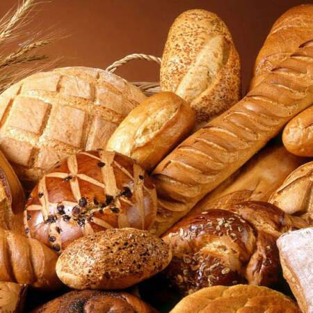 „Verschiedene frisch gebackene Brote und Brötchen in einem Korb, umgeben von goldenen Weizenähren.“